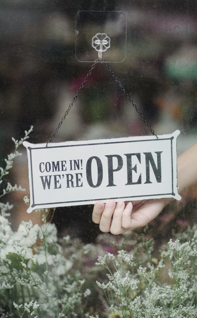 A welcoming open sign in a flower shop window with delicate blossoms in the foreground.