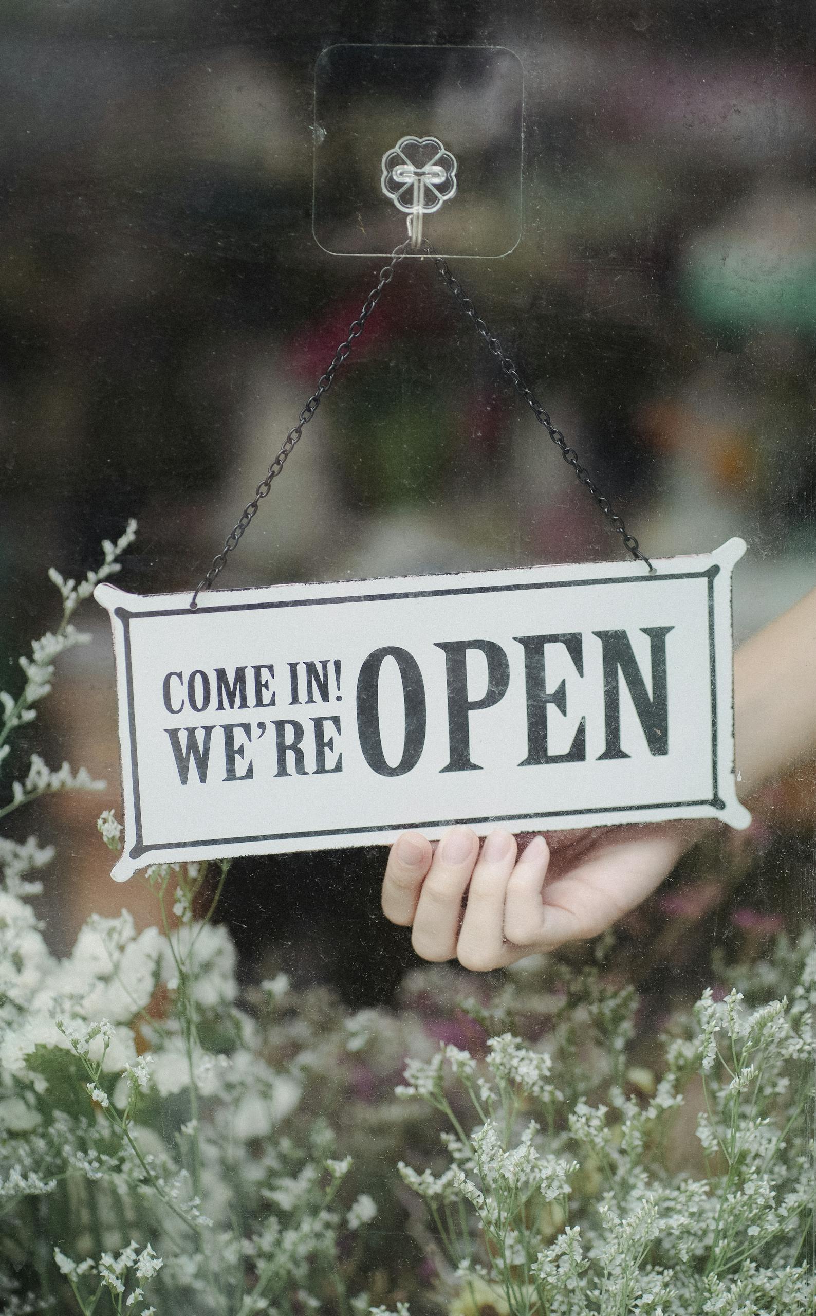 A welcoming open sign in a flower shop window with delicate blossoms in the foreground.